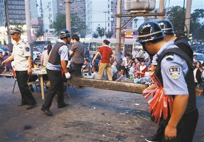 6月13日晚8點，朝陽路和青年路交叉口西側(cè)，一次聯(lián)合執(zhí)法行動中，輔警與協(xié)管抬走商戶的燒烤用具。新京報記者 尹亞飛 攝