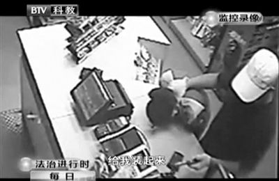 戴帽男子一手掐住加油站營業(yè)員，一手持發(fā)令槍指向另一營業(yè)員，要求“把錢給我裝起來”。