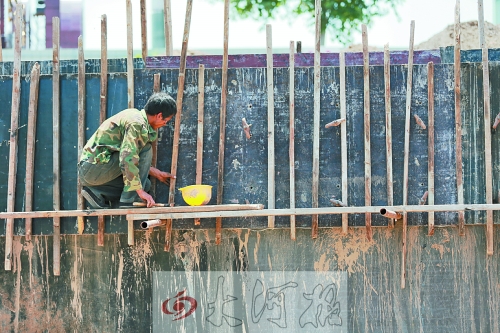 　　烈日下，狹窄的架子上，工人正用錘子固定樁基。