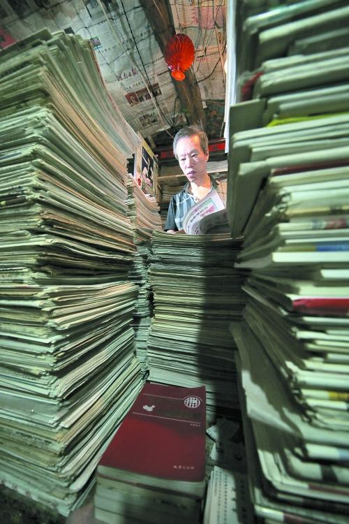 王曉民坐在寫字桌前，被報紙淹沒。