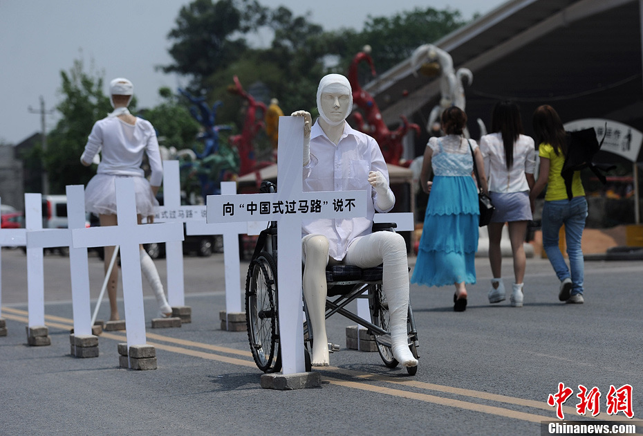 4月16日，重慶市洋人街上擺放著兩個受了傷的塑料人像“模特”，旁邊十字架上寫著向“中國式過馬路”說不