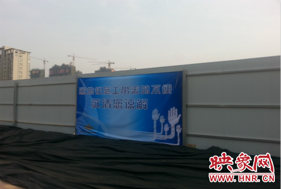 道路南側(cè)圍起了白色的圍擋，墻上標示著“因地鐵施工帶來的不便敬請您諒解”的提示牌。