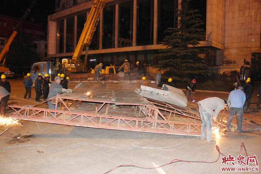 地面上的20多名工人對吊裝下的廣告牌進行分割。