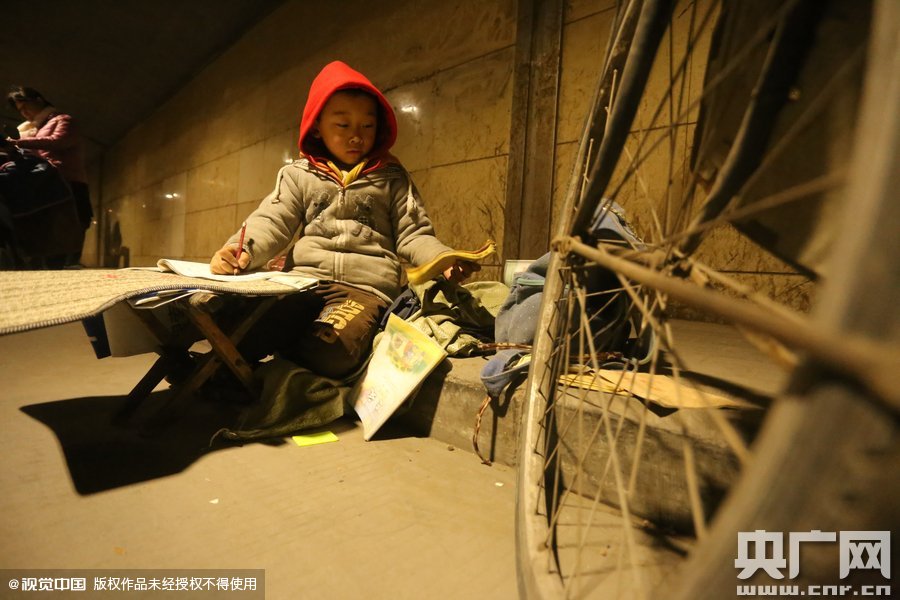 2015年11月8日晚，鄭州，7歲男孩涵洞橋下陪父母練攤，路邊燈下坐小馬扎上寫(xiě)作業(yè)。