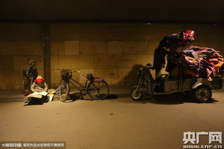 2015年11月8日晚，鄭州，7歲男孩涵洞橋下陪父母練攤，路邊燈下坐小馬扎上寫(xiě)作業(yè)。