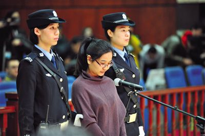 被告人盧梅低著頭，站在朝陽法院刑事審判庭的被告席上。