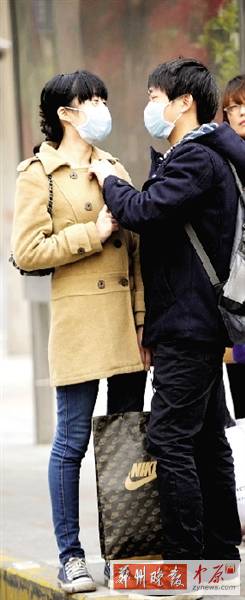 公交站臺上，一對年輕人戴著口罩，系緊衣領(lǐng)。